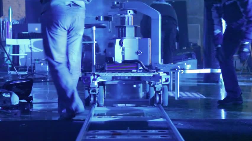 Workers dismantle rail cart for videocamera in room filled in with dark blue light close up