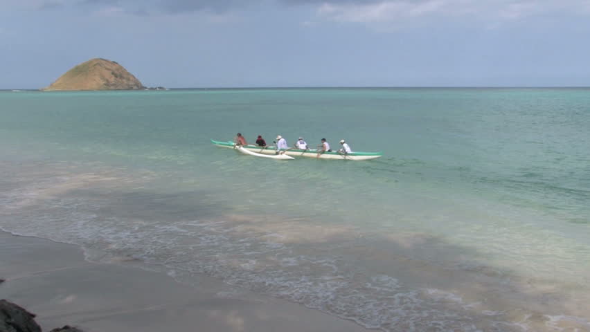 Tropical beach Oahu, Hawaii. Islands off shore in Pacific ocean. Outrigger paddling away from beach to another island. Waves on white sand with tree limbs overhead. Scenic, relaxing, calm seascape