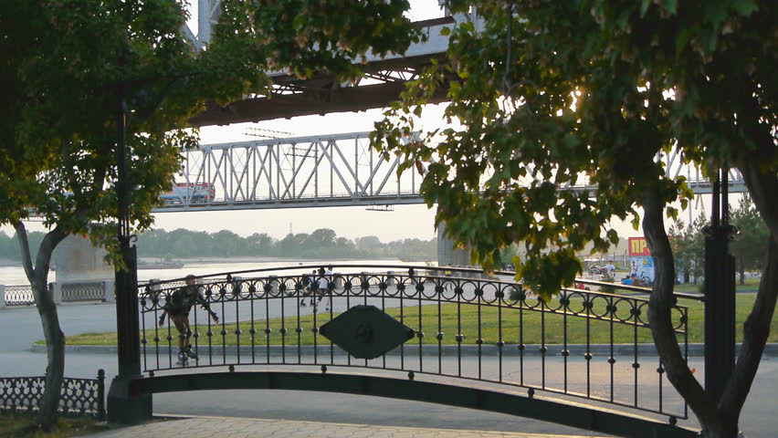 People resting at embankment. Train passing over a bridge.