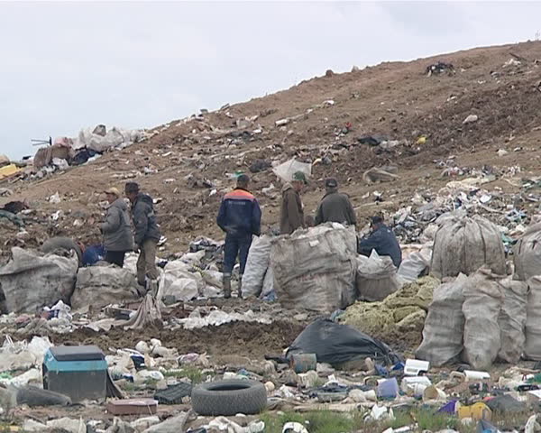 Many homeless people with full bags in dump surrounded by rubbish. Environmental pollution. Poverty. 