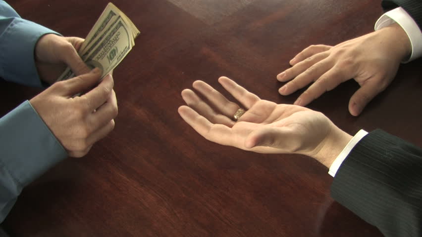 A man counts out hundred dollar bills into the hand of an impatient businessman, who taps his fingers on the table 