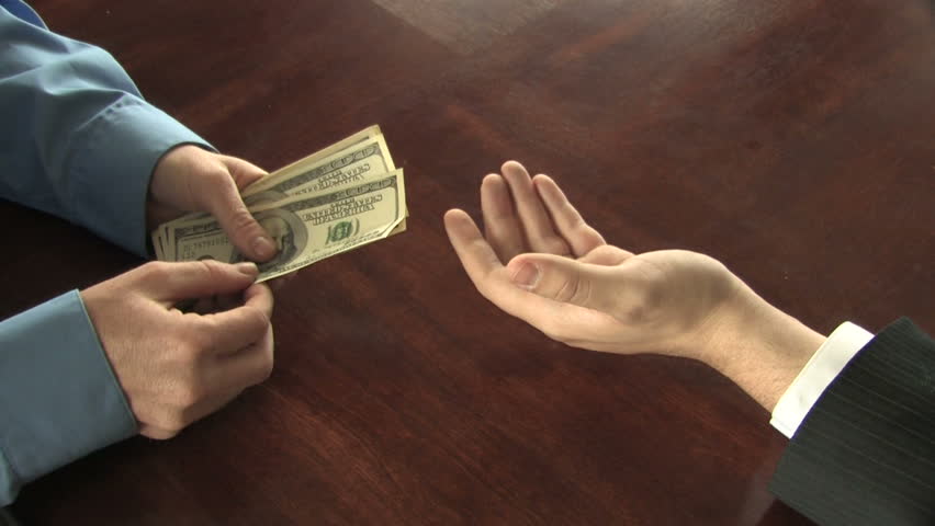 A man counts out hundred dollar bills into the hand of another businessman, who takes the money 