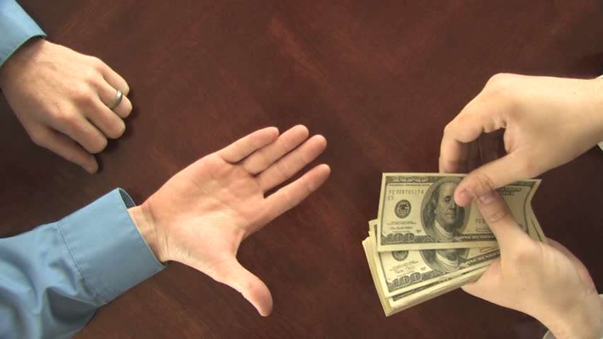 A manÃ¢â¬â¢s hand transfers hundred dollar bills to another manÃ¢â¬â¢s hand, over a table  