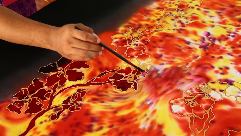 An artist carefully paint the flower motif on a reddish batik fabric with tiger-like pattern