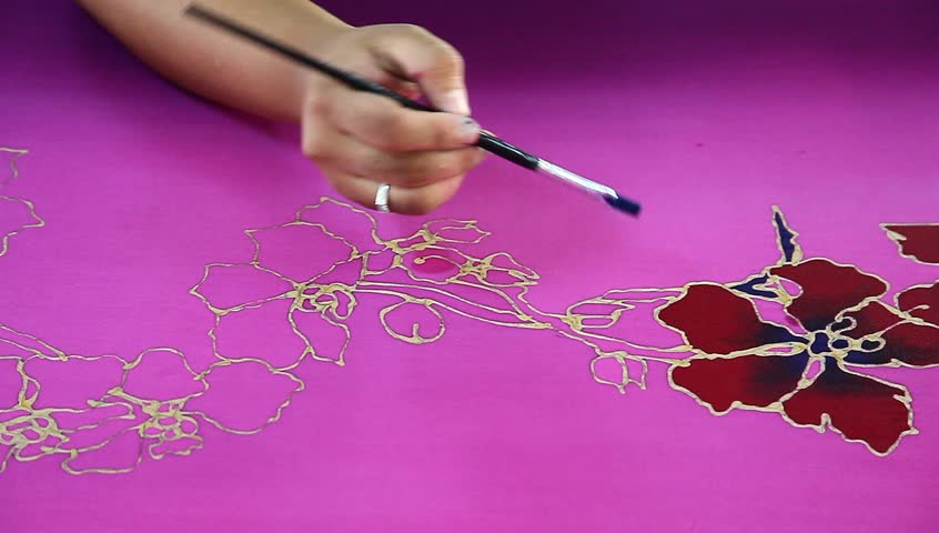 An artist carefully paint the flower motif on a pink batik fabric 