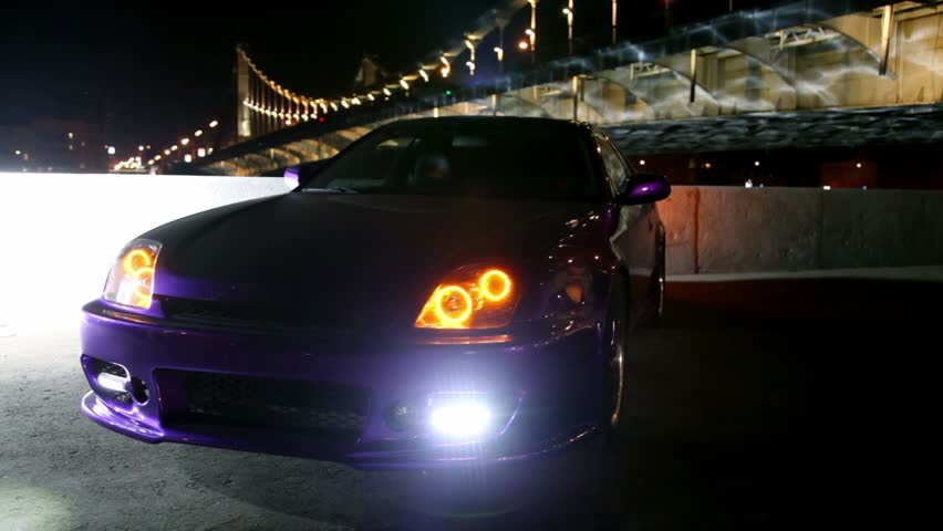 Car stand with parking lights blinks at background of bridge at night 