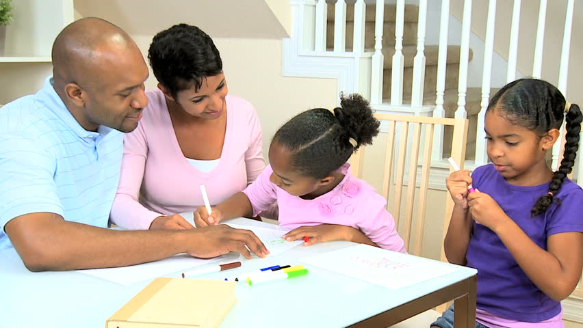 Young african american parents watching their cute young daughters using coloring crayons