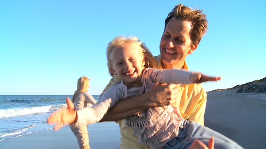 Young blonde parents having fun playing with their children on the beach