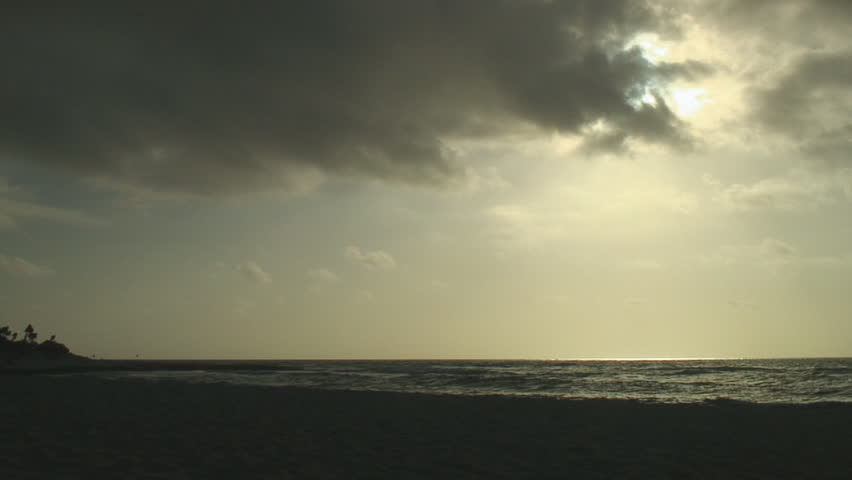 Sun emerges briefly from behind swift dark clouds to illuminate surface of ocean and shoreline