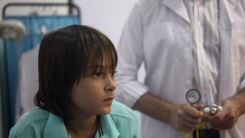 Friendly doctor at work and visiting with stethoscope sick child coughing in private medical clinic. Rack focus