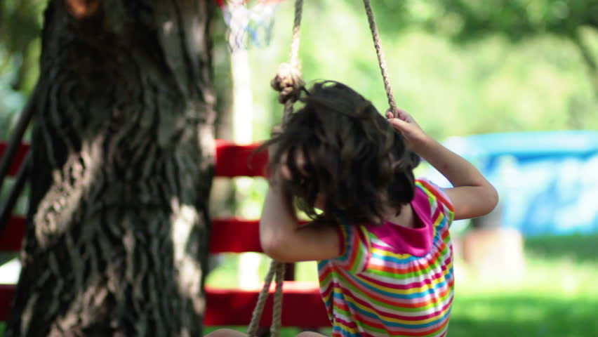 Young little  girl spinning in a tree swing and smiling