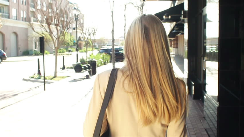 A pretty businesswoman walking with shopping bags turns around playfully smiling at the camera as she walks on.