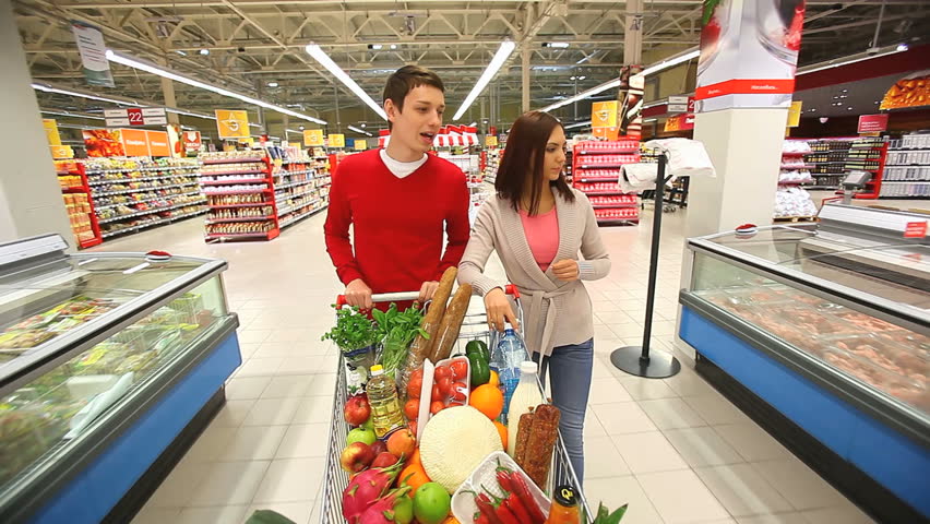 Cheerful couple walking through mall with a market trolley full of products