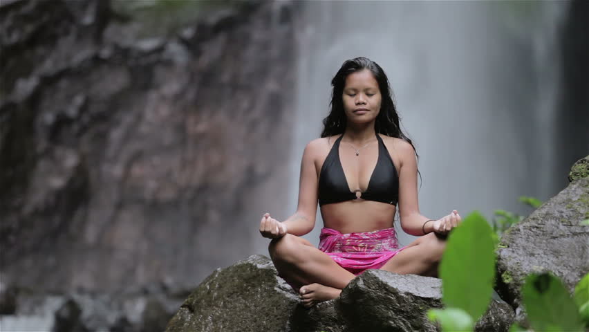 woman doing sitting meditation at waterfall in the tropics