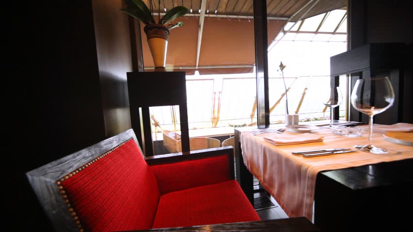 Decorated table for two with glassware and red chairs stand in a restaurant lounge, flying motion 