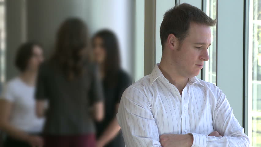 Male professional stands in front of coworkers - depressed