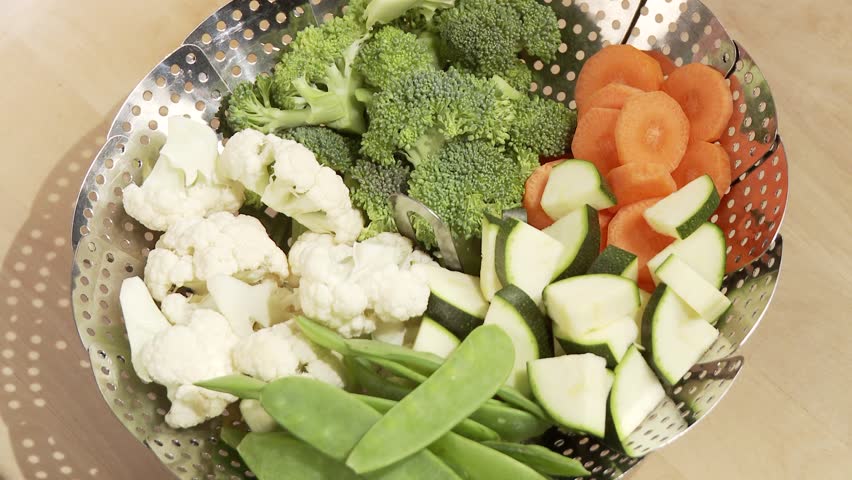 A steamer filled with vegetables being placed in a pot