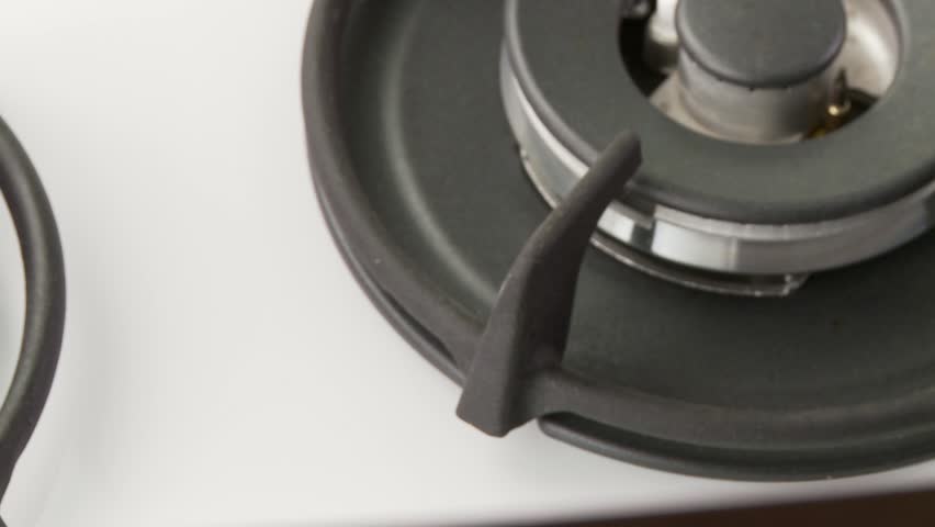 A gas cooked being turned on and a pot of water being placed upon it