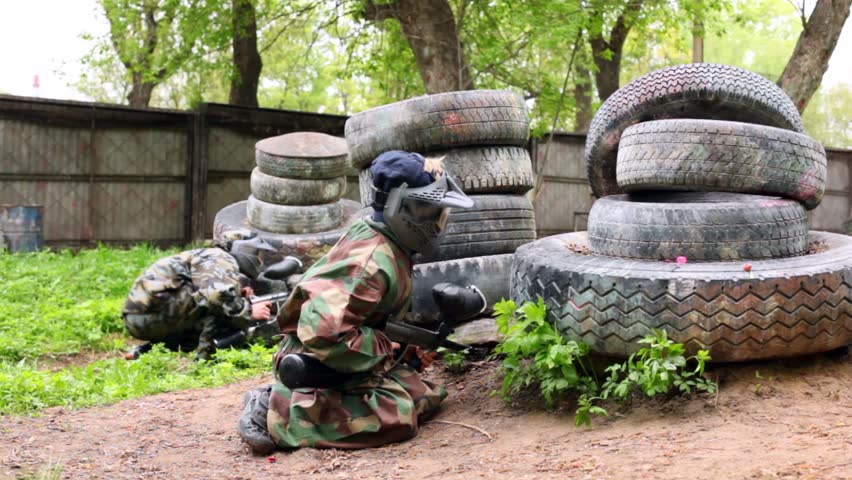Two boys paintball players sit in ambush behind pile of tires
