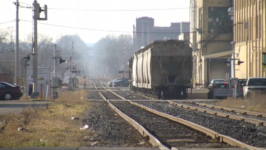 A freight train slowly moves down the track, pulling a small load. Various cars pass by in the foreground. (High Definition)