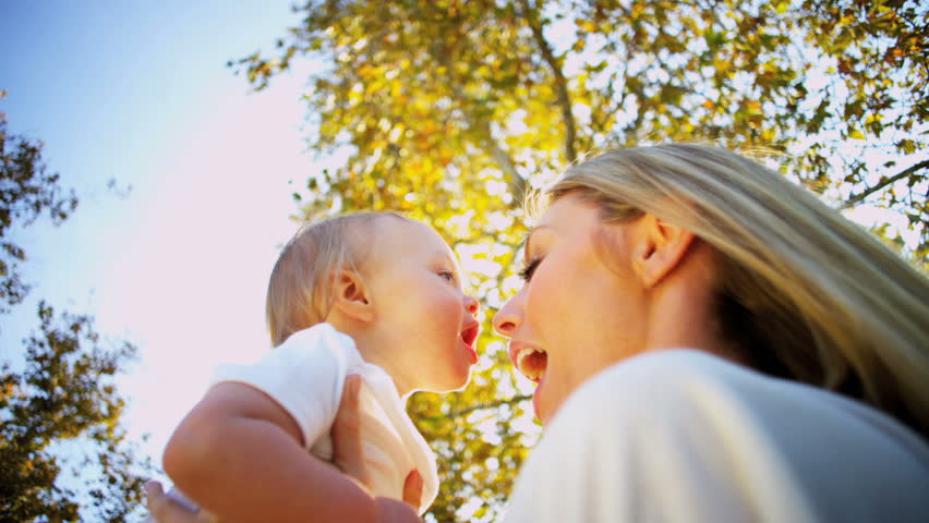Beautiful blonde mother and baby exchange a tender kiss as they play together outdoors
