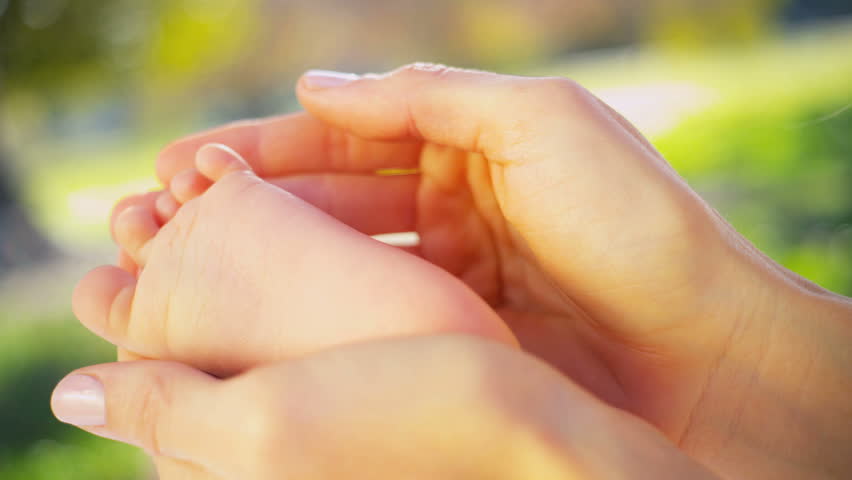Portrait in close up of a mothers hands holding the foot of her baby