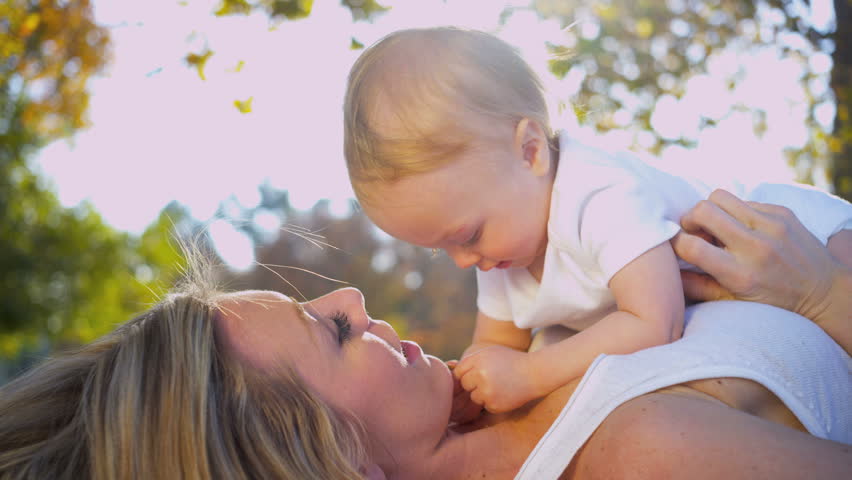Beautiful young mother in close up lying outdoors on the grass and tenderly kissing her baby