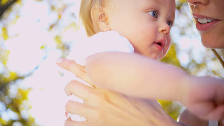 Portrait in close up of young blonde mother outdoors with her smiling baby