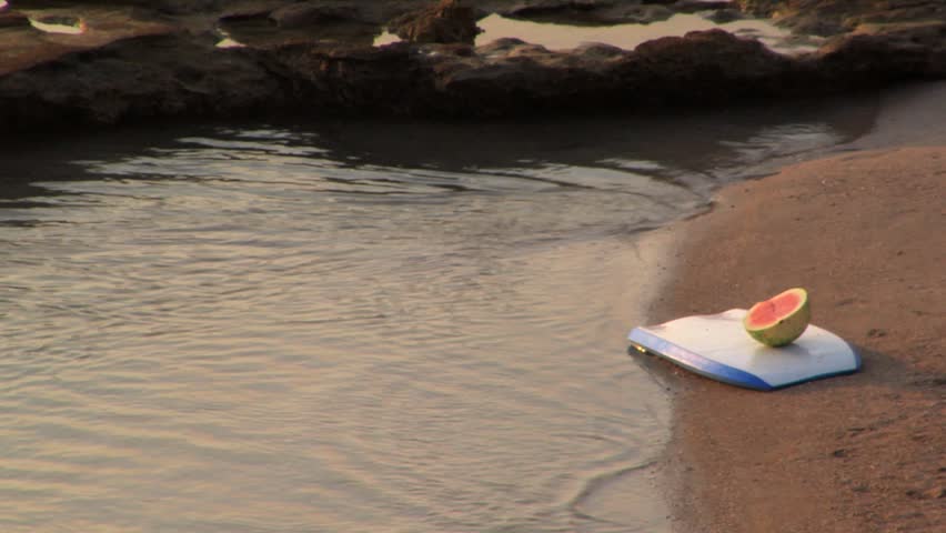 Open watermelon placed on a small surfboard on the beach
