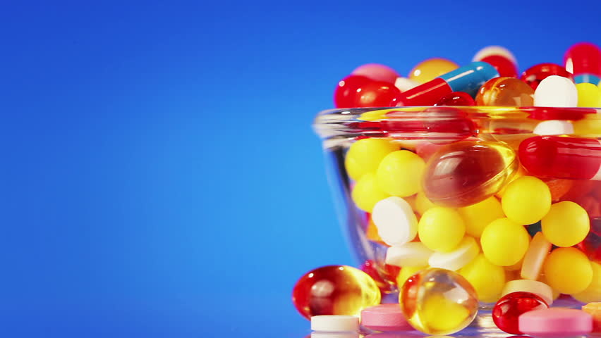 Pills, tablets and drugs in glass bowl rotating on blue background with copyspace - 2 views, loop ready