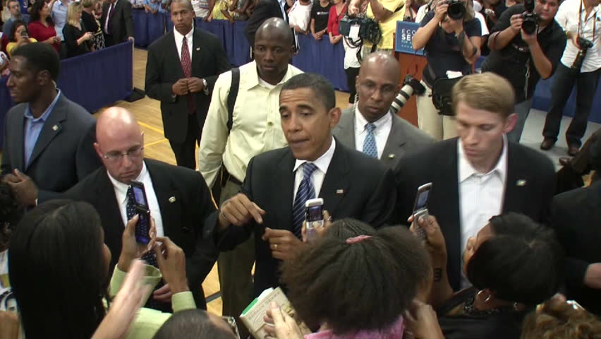 Barack Obama shakes hands surrounded by the secret service.
