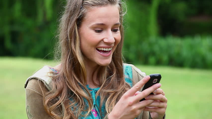 Happy young woman typing on her cellphone in a park