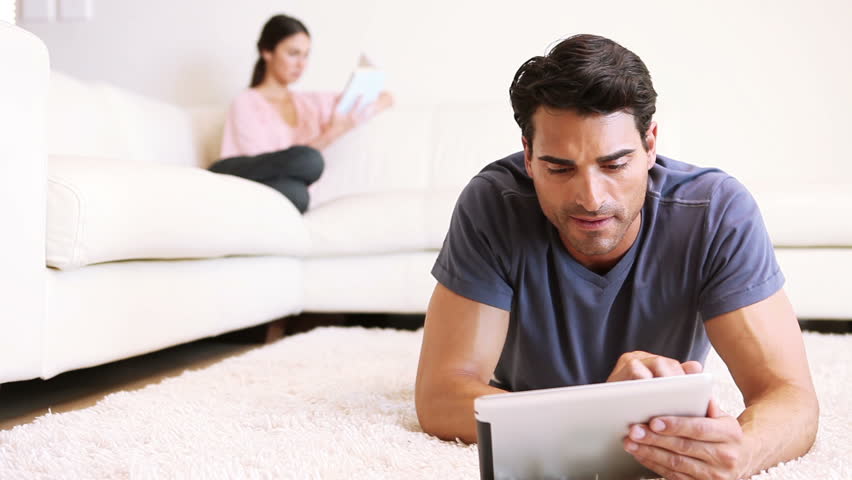Man touching his tablet computer while lying in his living room