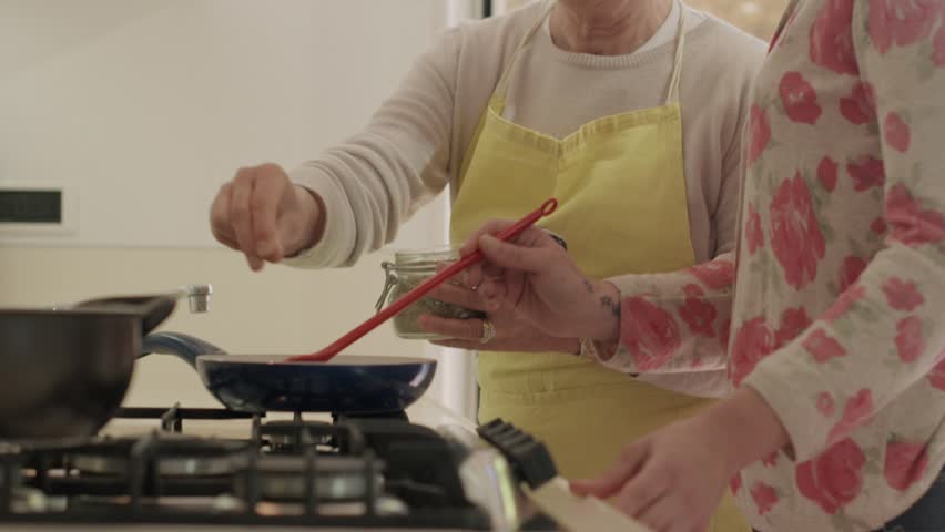 Senior and young woman, happy mother and daughter having fun while preparing food and cooking together in kitchen at home