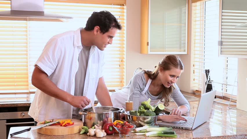 Man and woman use the laptop for a recipe while they are cooking in the kitchen