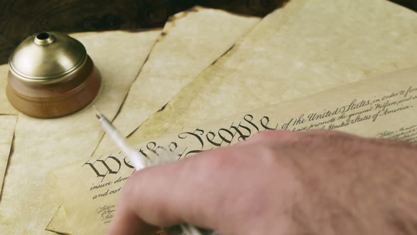 US Constitution Hand Reading (HD). US constitution parchment with feather quill shown with a male hand slowly reading as camera tilts down.