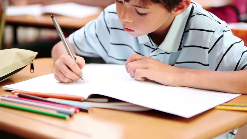 Smiling boy writing on his notebook in the classroom