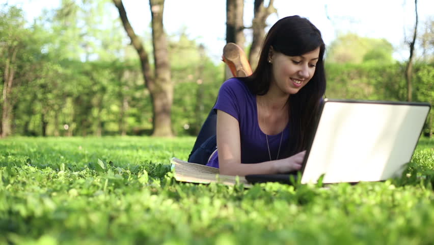 College student lying down on the grass and working on laptop, tracking shot