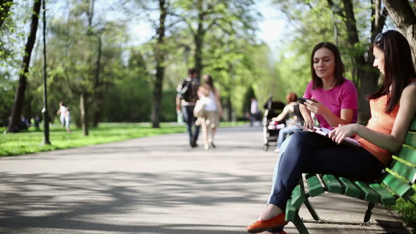 Two young college friends using a smart phone, outdoors, tracking shot