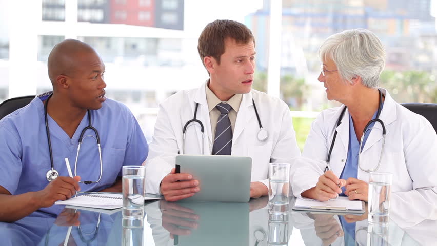 Serious doctor talking with his colleagues about a tablet pc in a bright room