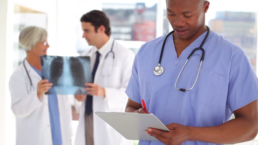 Nurse writing on a clipboard in front of doctors in a medical office
