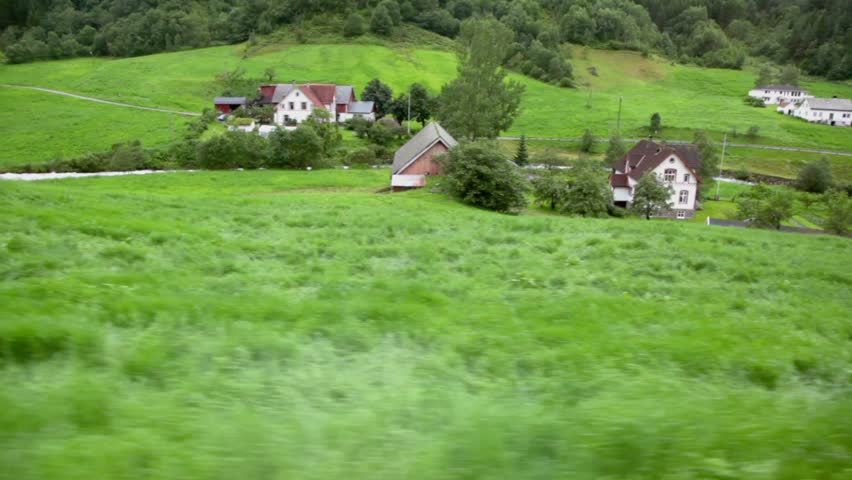 Small village near river among trees under mountain, shown in motion