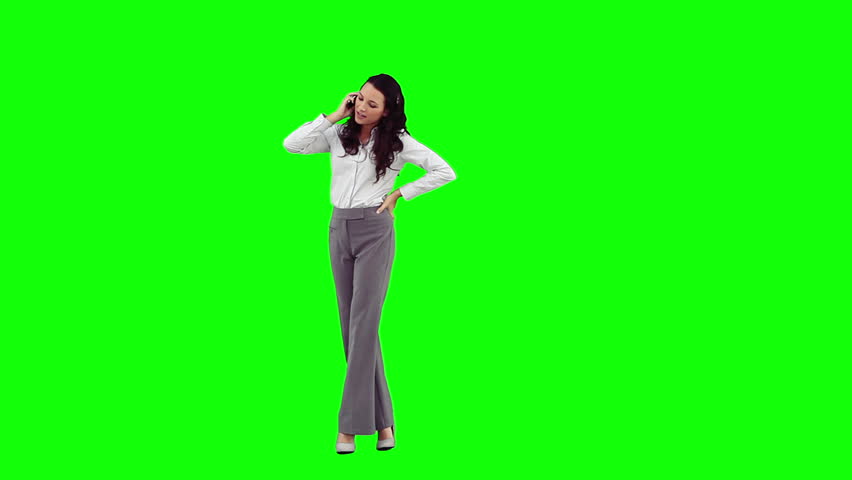 A businesswoman is having a conversation on her mobile phone in front of a green background