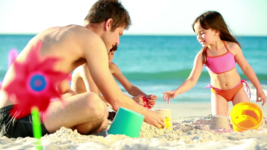 Children building sand castles with their father on the beach