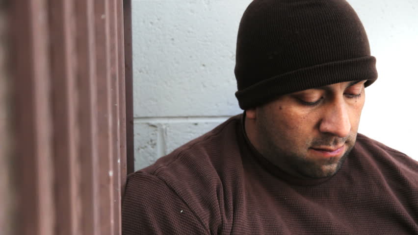 Homeless man sitting on the side walk looking at traffic go by