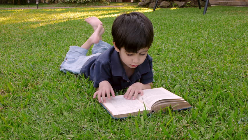 Kid Reading Book (HD)  Four year old boy of Hispanic origin flipping the pages of a book lying on a grassy patch.