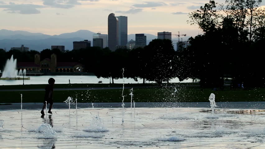 Child silhouette playing in a public water fountain, with the Denver, Colorado skyline in the background, at sunset. HD 1080p.