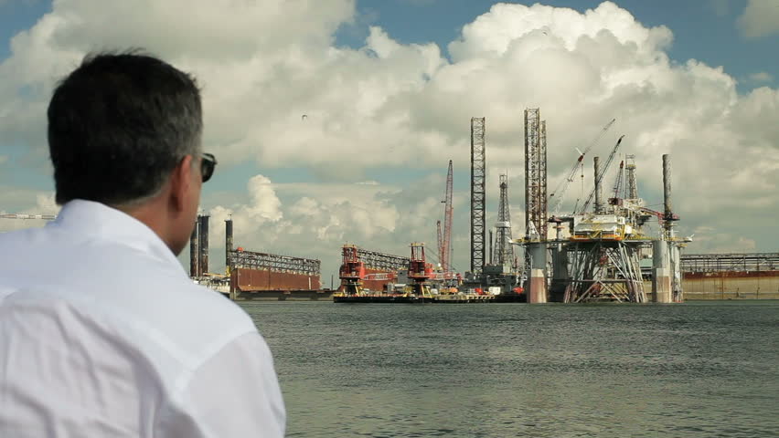 Man looking at oil platform in the distance and other marine activity.