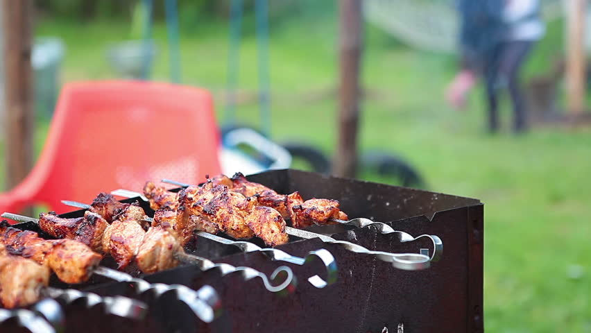 Smoking skewers on the grill and unrecognizable mother and daughter playing in the background