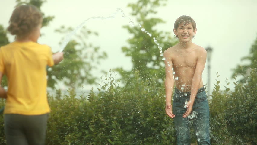 Girl pouring hose water over smiling boy